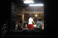夜の神社の室内で囃子方の人たちが囃子の練習をしている様子を遠くから写した写真