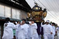 全身白い衣装を身に付けた人たちが神輿を担いで歩いている写真