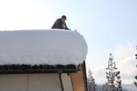 大雪が積もっている屋根の上に男性がいる写真