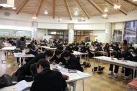 雄山中学校の沢山の生徒達がホールに設置された机に向かって勉強に取り組んでいる放課後学習教室の写真