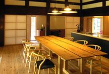 天井は大きな梁の柱が見える現代風のキッチンに6人がけのテーブルと椅子が置かれている写真