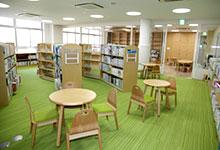 本が綺麗に整理された本棚が並んでおり、テーブルと椅子があちらこちらに設置されているグリーンの絨毯が敷かれた図書館の写真