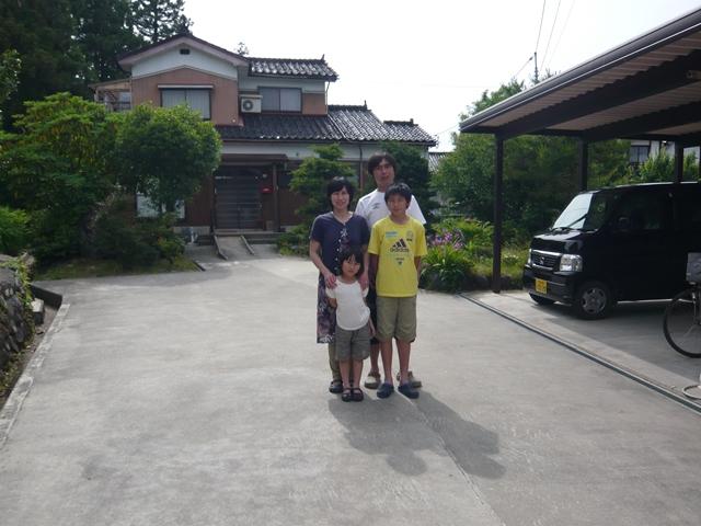 自宅の車庫の前で家族4人が並んで写っている川端さん家族の写真