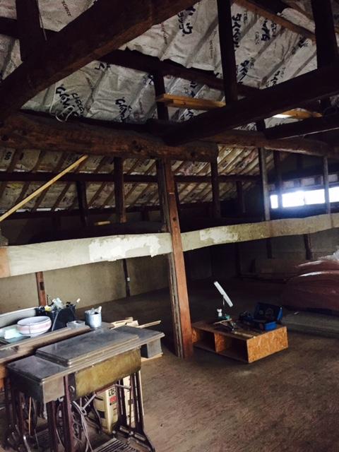 屋根裏の天井には白いシートが貼られ梁が見えており、古いミシンなどが置かれ綺麗に整理されている屋根裏の写真