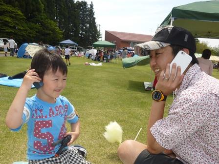 芝生が生えた広場に座って男の子と一緒に電話ごっこをしているお父さんの写真