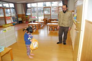 女の子が手に持っている黄色のカバンを覗き込んでいる様子を少し離れたところから見ているお父さんの写真