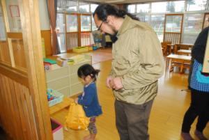 黄色のカバンを持った女の子の横に立って女の子の方を見ているお父さんの写真