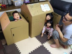段ボールで出来た家で遊んでいる子供達を見ているお父さんの写真