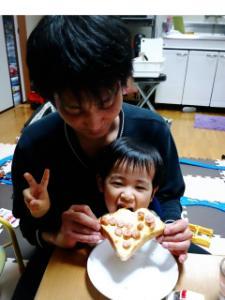 子供を膝の上に乗せて具がのった食パンを食べさせているお父さんの写真