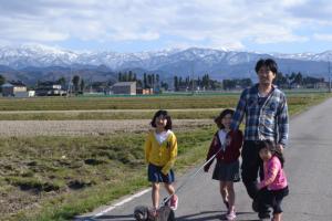 雪が積もった立山連峰が奥に見える道で犬の散歩をしている女の子3人とお父さんの写真
