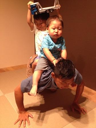 男の子2人が四つん這いになっているお父さんの背中に乗っている写真