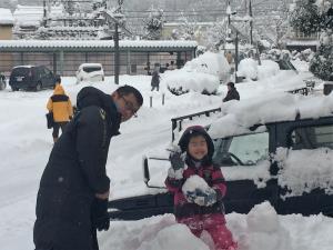 辺り一面雪が積もっており、お父さんと女の子が雪だるまを作っている写真