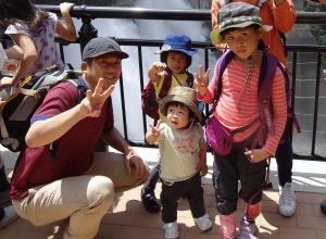 奥にダムの水が放水しているのが見える場所で記念撮影をしている女の子3人とお父さんの写真