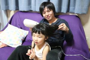 女の子の髪の毛をドライヤーで乾かしているお父さんの写真