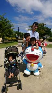 公園でベビーカーに乗っている男の子と、キャラクターの置物の後ろにいる男の子2人とお父さんが写っている写真