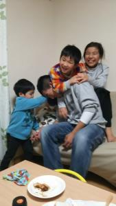 ソファーに座っているお父さんに子供達3人が群がっている写真