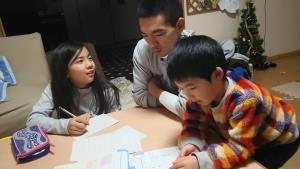 女の子と男の子が座っているテーブルで一緒にプリントを見ているお父さんの写真