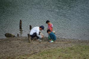 水辺で男の子2人とお父さんがしゃがんで何か作業をしている写真