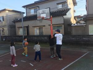 屋外で子供達とバスケットをしているお父さんの写真