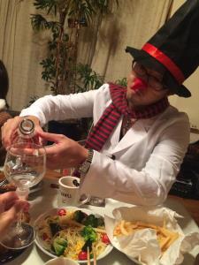 シルクハットを被り、赤と黒の縞模様のマフラーを巻き、赤い花を付けたお父さんが飲み物をグラスに注ごうとしている写真