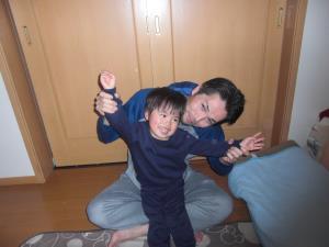 男の子を足の上に乗せて床に座ってポーズを取っているお父さんと男の子の写真