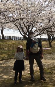 女の子と手をつなぎ、小さい子を抱っこして桜の木の下に立っているお父さんの写真