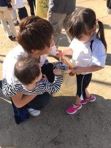 赤ちゃんを抱っこしているお父さんが女の子の目線に合わせて女の子の方を向いている写真