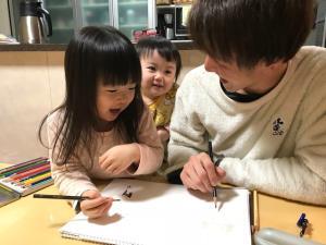 女の子とお父さんが同じ画用紙に一緒に絵を描いている写真
