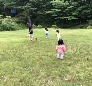 お父さんと女の子3人が広い原っぱを駆け回っている写真