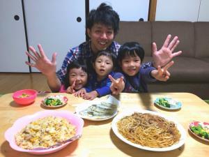 テーブルに並べられたチャーハンや焼きそばを前にして子供達3人とお父さんが一緒に笑顔で写っている写真