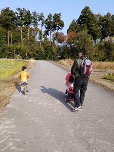自転車に乗っている男の子と、ベビーカーを押して散歩をしているお父さんの後ろ姿の写真