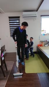 掃除機をかけているお父さんの後を付いて行っている男の子2人の写真