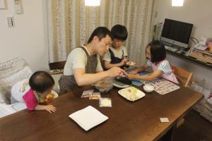 テーブルでエプロンを付けた子供達とお父さんが一緒に餃子を作っている写真
