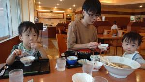 レストランで子供達の間に座り、右側の男の子に食事をさせているお父さんの写真