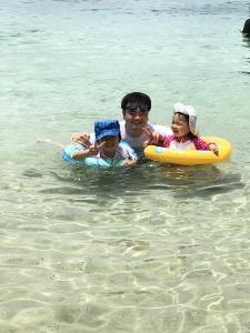 浮き輪に入った子供達と一緒に海で泳いでいるお父さんの写真