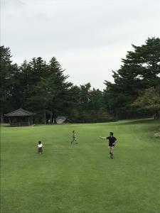 芝生が生えた広々とした広場で子供達2人と遊んでいるお父さんの写真