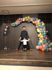 沢山の風船で出来たアーチの下で子供と写真を撮っているお父さんの写真
