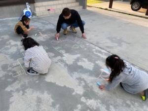 子供達と一緒に地面にチョークで絵を描いているお父さんの写真
