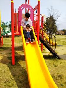 公園の滑り台を子供と一緒に滑っているお父さんの写真