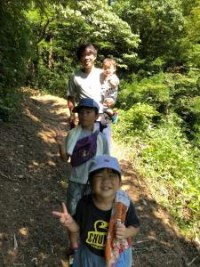 赤ちゃんを抱っこして、子供達2人と自然に囲まれた道を歩いているお父さんの写真