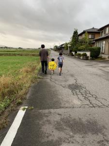 お父さんと男の子2人が田んぼ横の道路を歩いている後ろ姿の写真