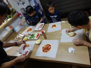 子供達3人とお父さんがテーブルの上でピザを作っている写真