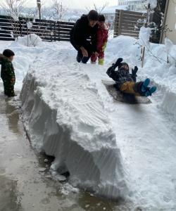 雪で出来た坂で1人の子供が坂を滑っているのを見ている子供二人とお父さんの写真