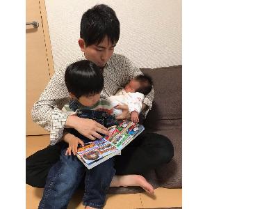 子供たちを膝にのせて絵本を読んでいるお父さん
