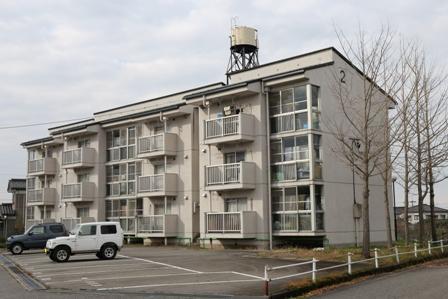 3階建て12戸の上米沢町営住宅と住宅の前には駐車場があり、2台の車が停まっている上米沢町営住宅の写真