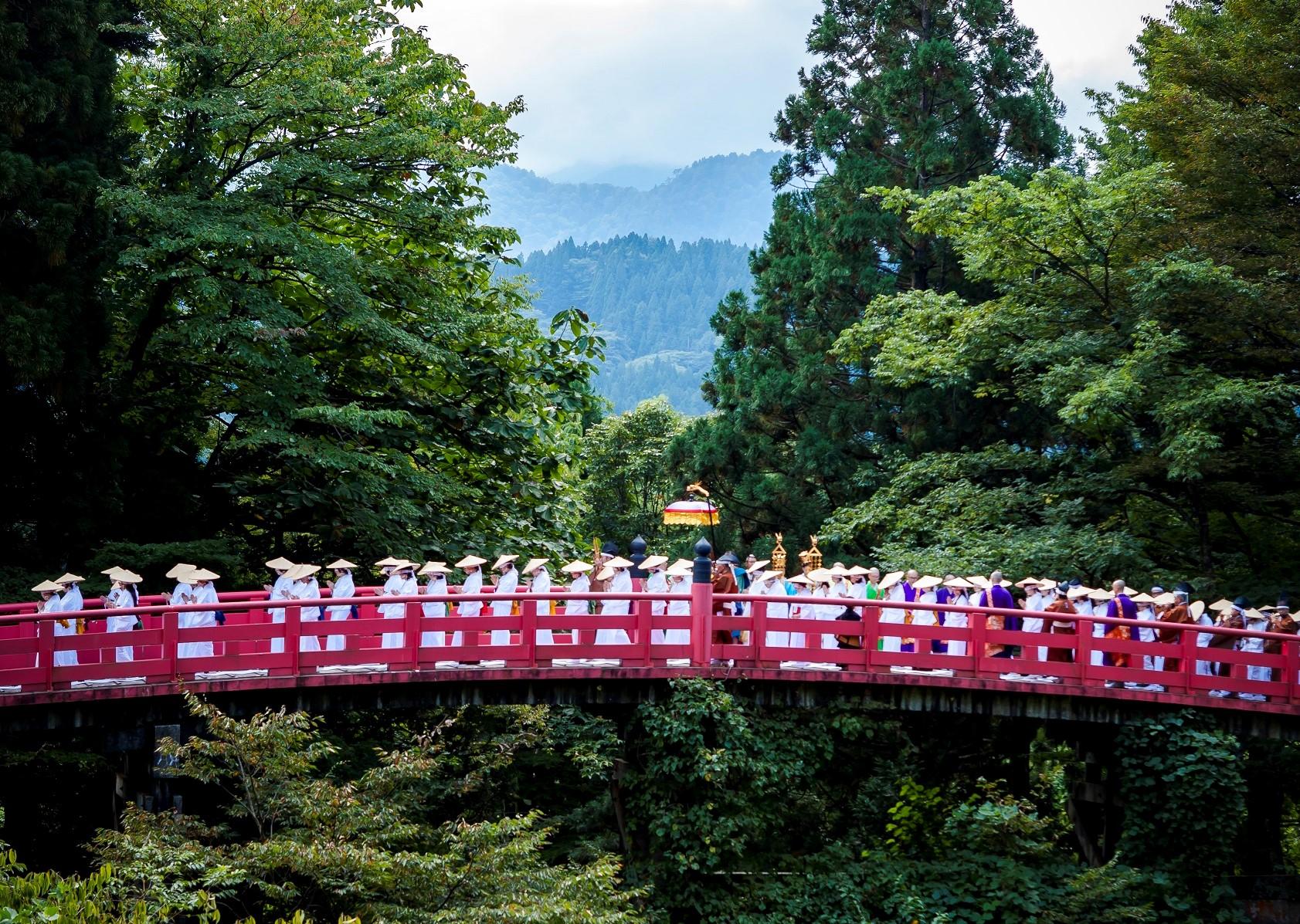 白装束にすげ笠を被っている女性達や僧侶が朱塗りの橋を歩いている布橋灌頂会の写真
