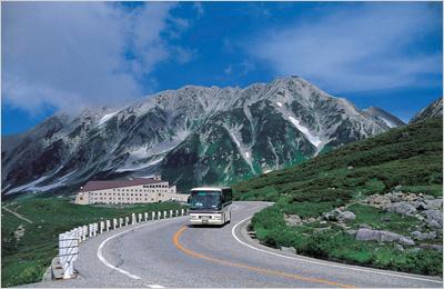 山のきれいな景色が見える道路を1台のバスが通っており、後方の山々に雪が降り積もっている写真