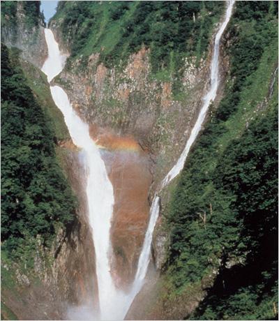 岩場を水しぶきを上げながら二股に別れている水が一つになって流れ落ちる滝の写真